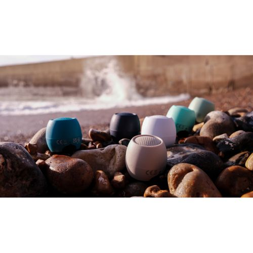 Plusieurs petits haut-parleurs ronds de différentes couleurs sont sur une plage de galets.
