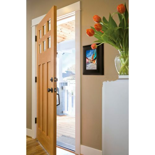 Una puerta de madera abierta conduce a un área exterior luminosa con tulipanes y un cuadro.