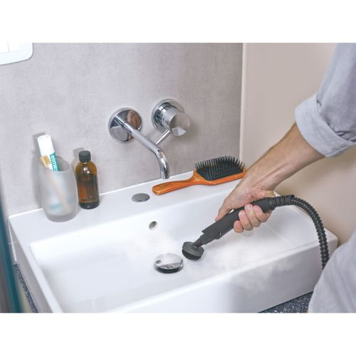 Una persona pulisce un lavandino con un pulitore a vapore.