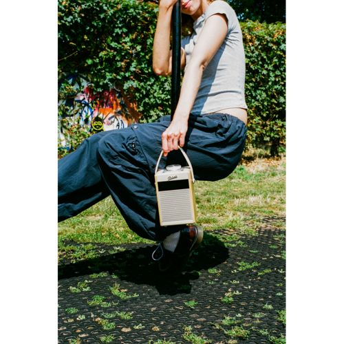 Personne sur balançoire tenant une enceinte portable beige, fond vert.