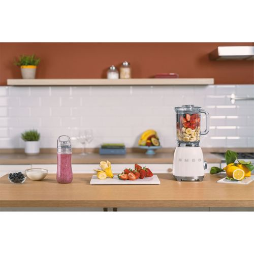 Ein weißer Smeg-Standmixer mit Früchten, daneben ein Smoothie und Zutaten.