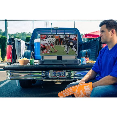 Ein Mann sitzt auf der Heckklappe eines blauen Pickups und schaut auf einen Fernseher, der Football zeigt.