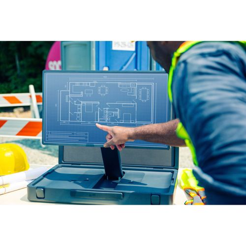 Ein Mann in Arbeitskleidung zeigt auf einen Bauplan auf einem Bildschirm im Freien.
