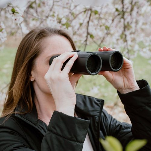 Una donna guarda attraverso un binocolo con fiori bianchi sullo sfondo.