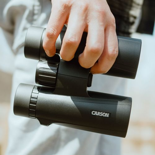 Una mano tiene un binocolo nero marca Carson.