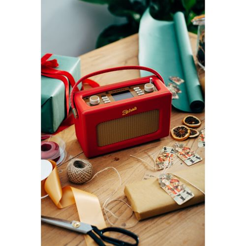 Ein rotes Retro-Radio mit Griff, Geschenken und Bastelmaterial auf einem Holztisch.