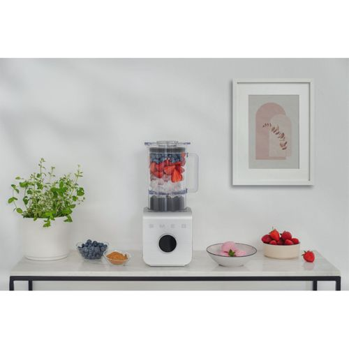 Un frullatore bianco con fragole, mirtilli e cubetti di ghiaccio su un piano di marmo.