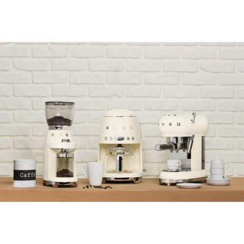 Tres electrodomésticos SMEG color crema: molinillo, cafetera de goteo, máquina de espresso.