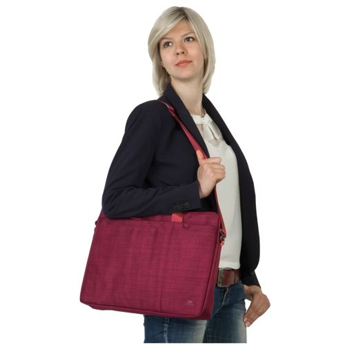 Eine Frau mit kurzblondem Haar trägt eine dunkelblaue Jacke und eine weinrote Laptoptasche.
