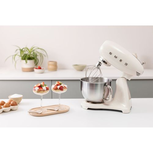 Una batidora de pie Smeg color crema con varillas junto a dos postres con fresas y nata.