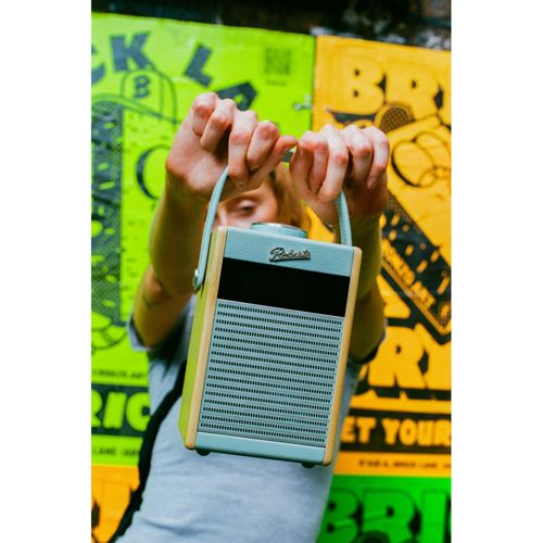 Une personne tient une enceinte bleu clair et en bois devant de l'art graffiti coloré.