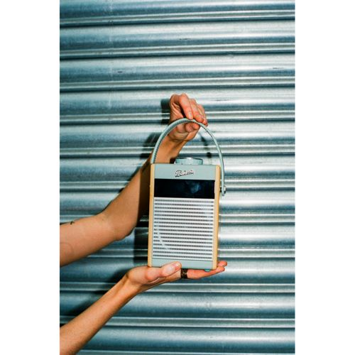 Personne tenant une radio bleu clair avec cadre en bois et poignée devant un mur nervuré.