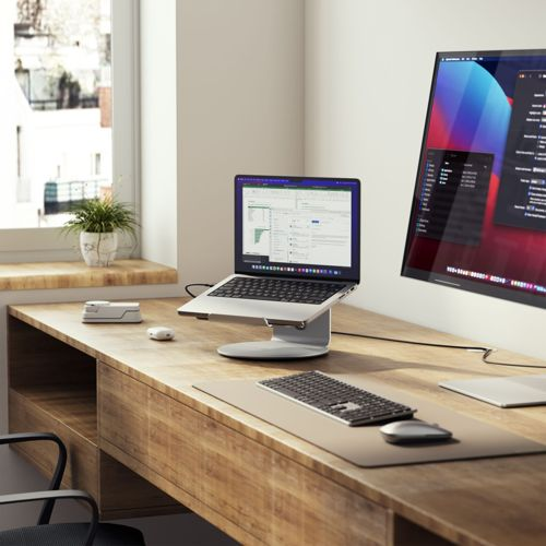 Ein moderner Schreibtisch mit Laptop, externem Monitor, Tastatur, Maus und Pflanze.
