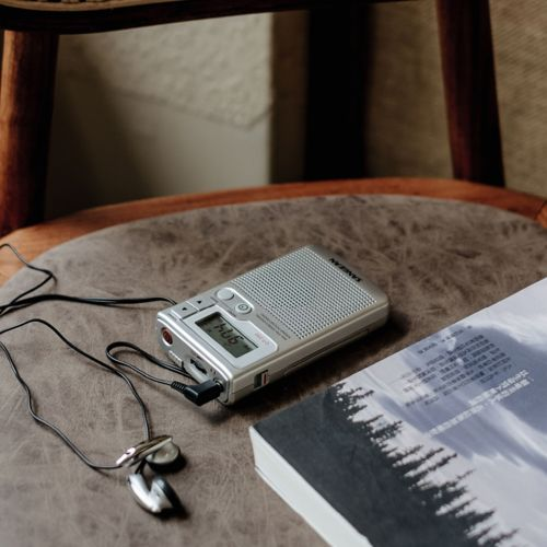 Un grabador plateado con auriculares y un libro en una silla marrón.
