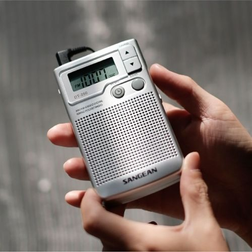 Persona sosteniendo una radio plateada pequeña con pantalla LCD y altavoz.