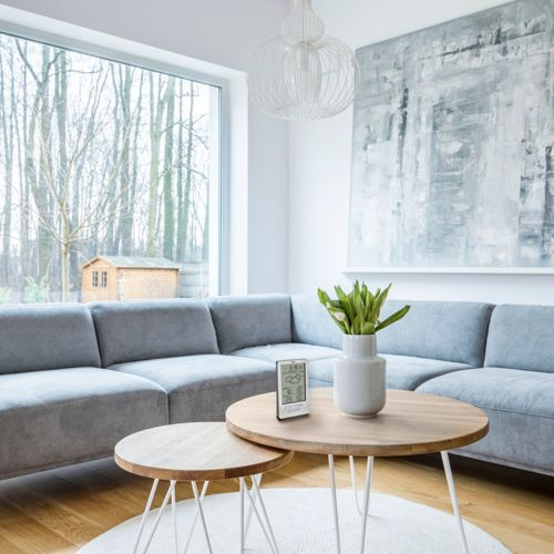 Ein moderner Wohnraum mit einem grauen Ecksofa, Holztischen und einem digitalen Thermometer.