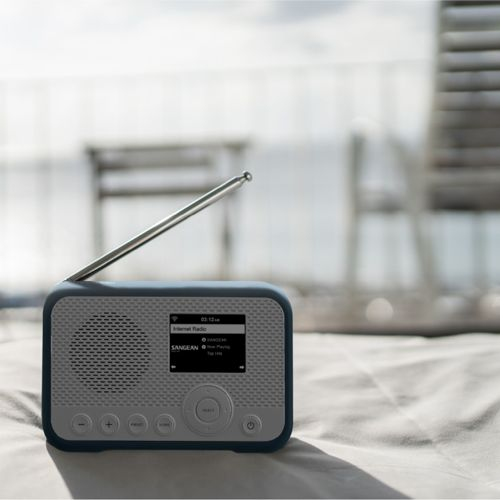 Een blauw-grijze internetradio met uitgeschoven antenne staat op een witte deken.