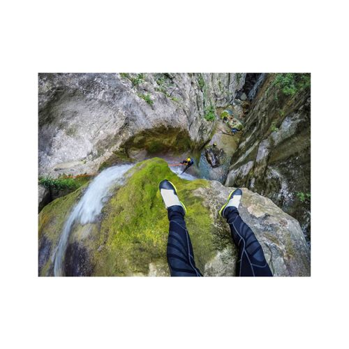 Persona seduta sul bordo roccioso sopra la cascata, gambe tese.