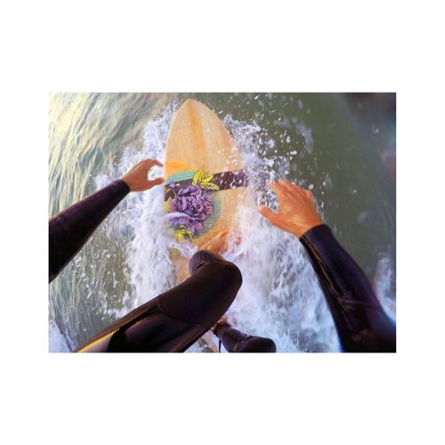 Surfer in muta su tavola da surf, mani sulla tavola, acqua che schizza