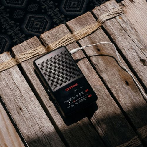 A black radio with headphone cord lies on wooden planks tied with rope.