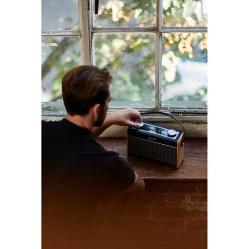 Homme règle le bouton d'une radio en bois devant une fenêtre.