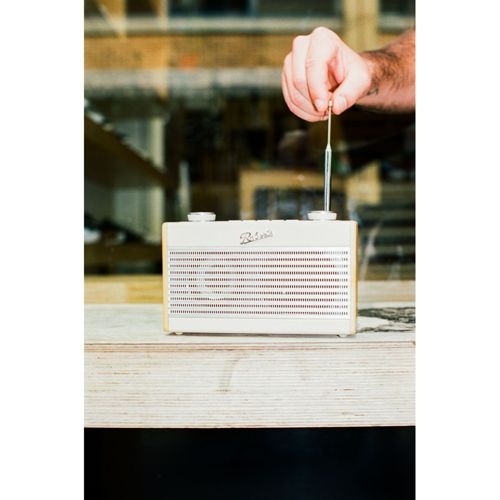 Un homme ajuste l'antenne d'une radio rétro blanche sur une table en bois.