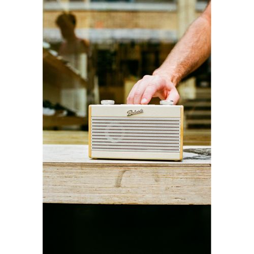 Un homme ajuste une radio Roberts couleur crème sur une table en bois.
