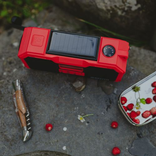 Rotes Solarradio, Messer und Erdbeerdose auf Steinen.