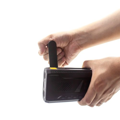 A hand holds a black device with an antenna. The other hand grips the bottom.