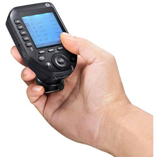 Una mano tiene un trigger per flash di fotocamera nero con schermo blu che mostra le impostazioni.