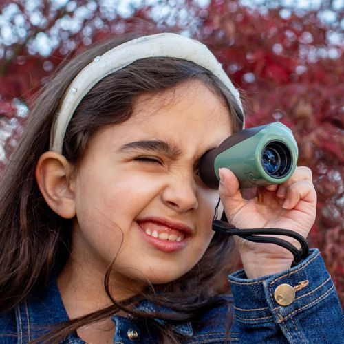 Una ragazza con una fascia guarda attraverso un monocolo verde e marrone.