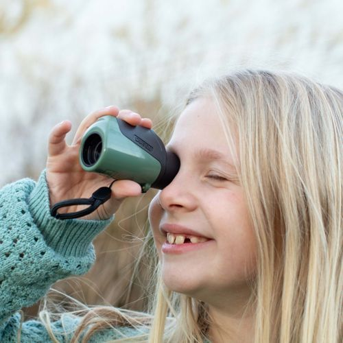 Una bambina guarda attraverso un piccolo monocolo verde all'aperto.