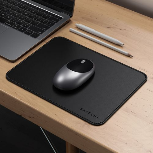 Ein silberner und schwarzer Maus auf einer schwarzen Unterlage neben einem Laptop und Stiften.