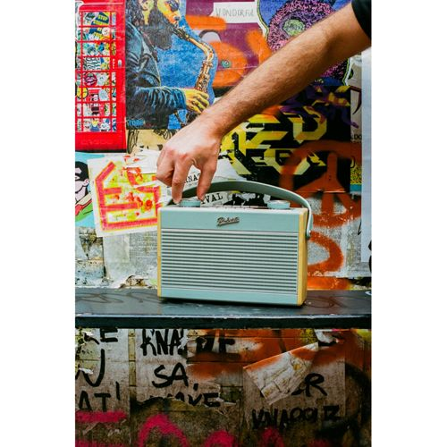 La main d'un homme ajuste une radio rétro bleu clair avec garniture en bois. Fond graffiti.
