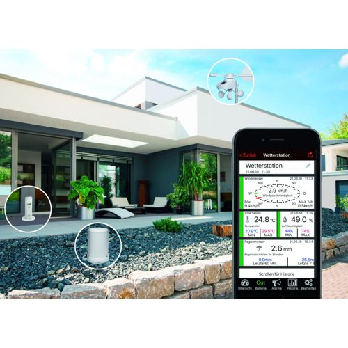Un smartphone affiche des données météorologiques devant une maison moderne avec des stations météo extérieures.