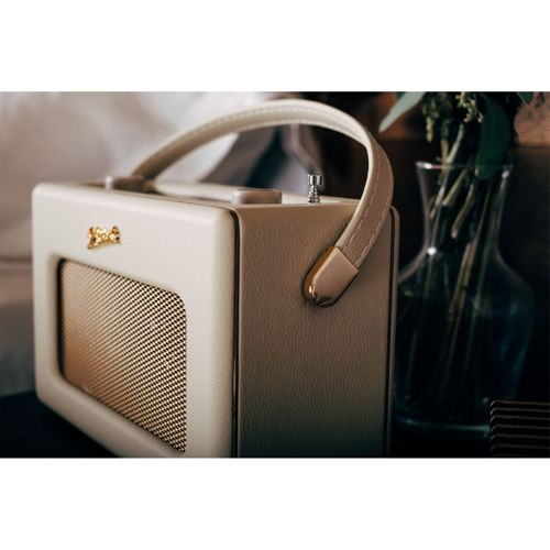 Ein cremefarbener Retro-Lautsprecher mit goldenem Gitter und Griff, daneben eine Vase.
