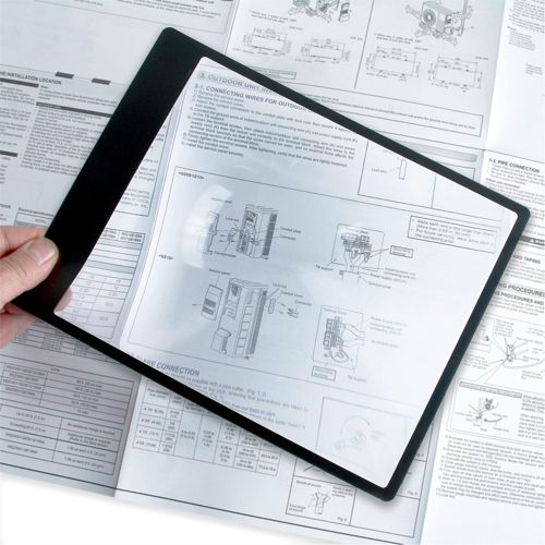Eine Hand hält eine schwarze Lupe über ein technisches Handbuch mit Diagrammen und Text.