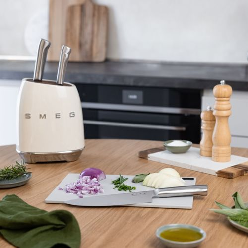 Ein cremefarbener Messerständer von SMEG mit zwei Messern steht auf einem Holztisch.