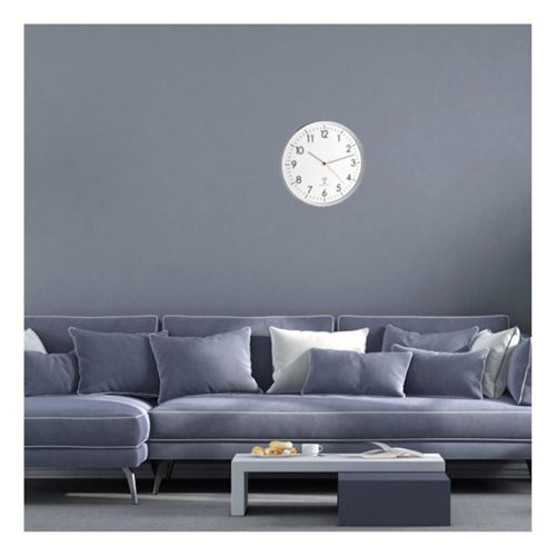 Eine graue Wand mit einer runden Wanduhr und einem blauen Sofa davor.