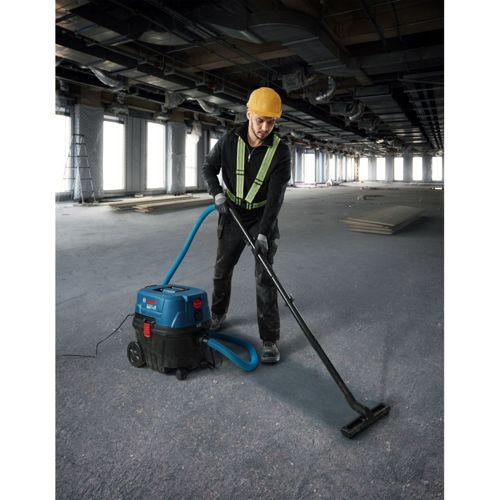 Operaio edile aspira pavimento con aspiratore Bosch blu in grande sala.