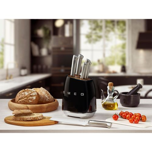 Ein schwarzer Messerständer mit Messern, Brot, Olivenöl und Tomaten auf einer Arbeitsplatte.