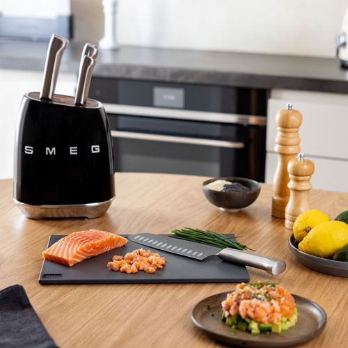Ein schwarzer Messerständer von Smeg mit Messern, Lachs auf einem Schneidebrett, Gewürzstreuern und Zitronen.