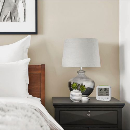 Ein Nachttisch mit Lampe, Vase und Digitaluhr neben einem Bett.