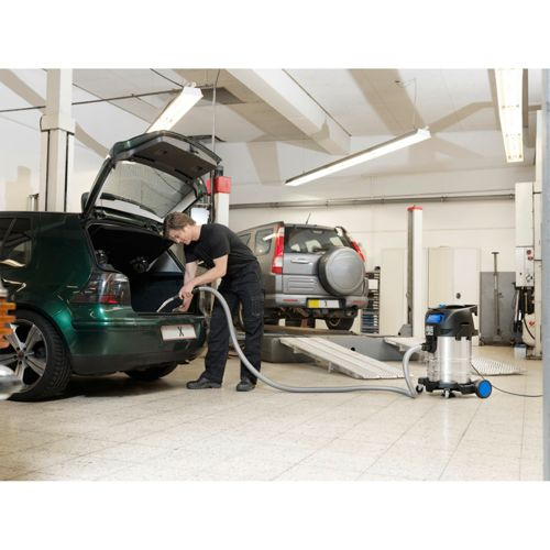 Ein Mann saugt einen grünen Kombi in einer Werkstatt aus. Ein grauer SUV steht daneben.
