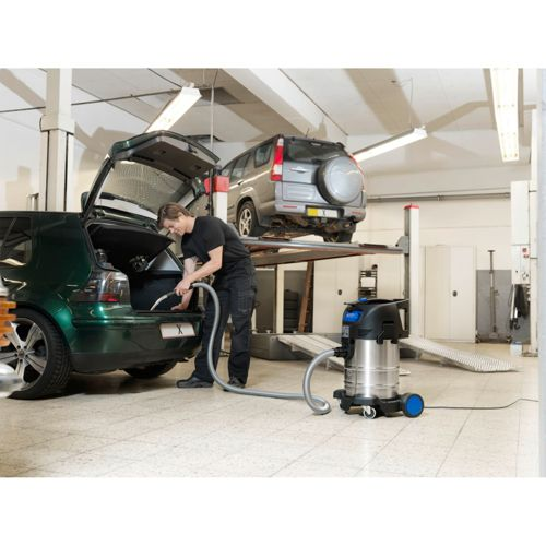 Ein Mann saugt einen grünen Kofferraum aus, während ein Auto auf einer Hebebühne steht.