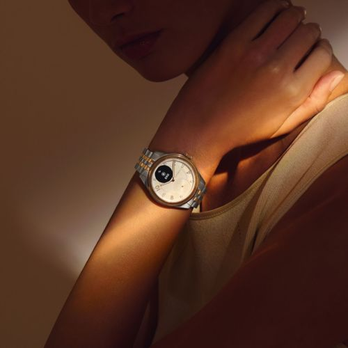 Primo piano di un polso con uno smartwatch argento e oro dal quadrante bianco.