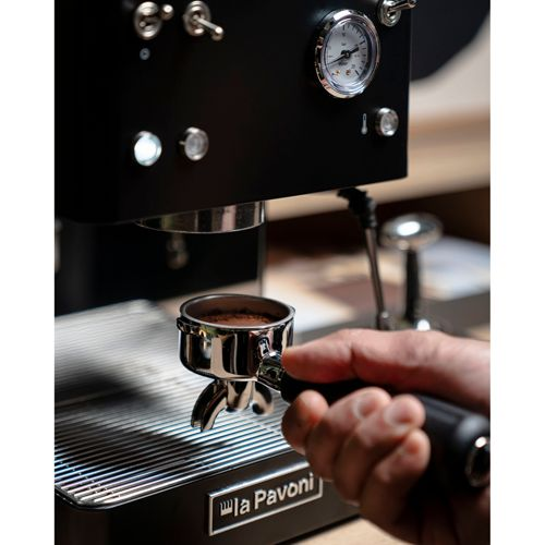 Eine Hand hält einen Siebträger mit Kaffeepulver unter einer schwarzen Espressomaschine.