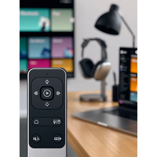 Un telecomando nero poggia su un tavolo di legno davanti a uno schermo TV sfocato.