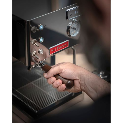 Eine Hand hält einen Holzgriff einer Espressomaschine, um Kaffee zuzubereiten.