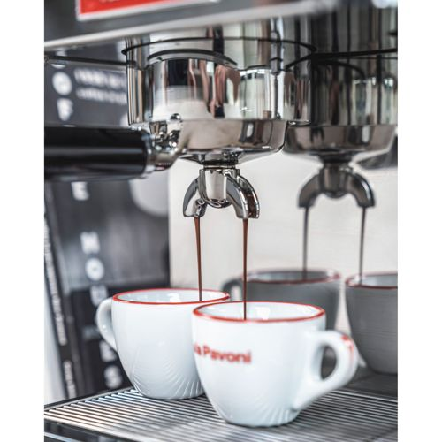Espressostrahl fließt in zwei weiße Tassen mit rotem Rand.